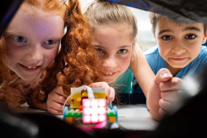 Two young girls and a boy look excitedly at a science project.