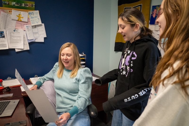 Two students look at their teacher reading.
